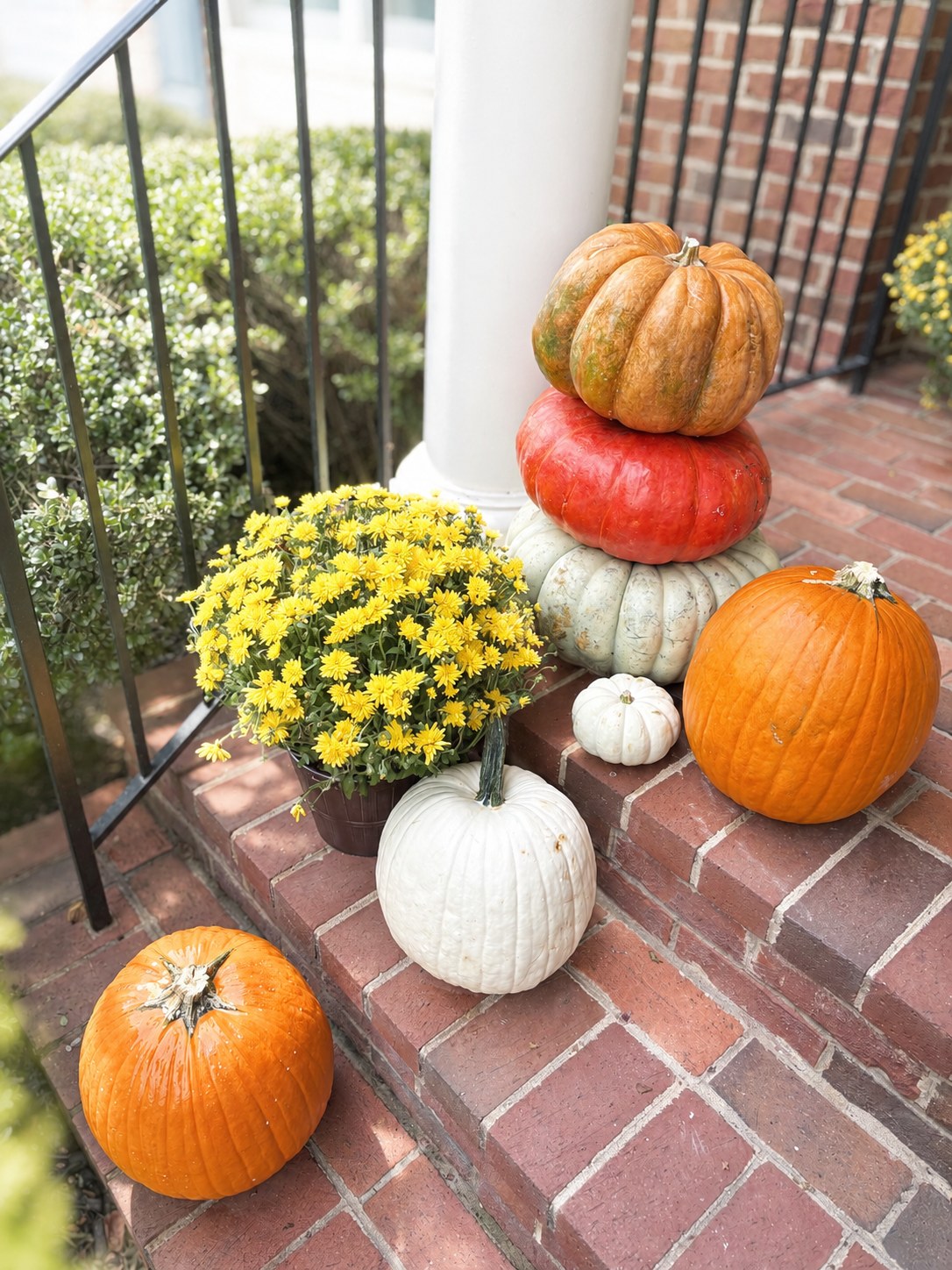 A three-high stack of heirloom pumpkins at the foot of a white porch column